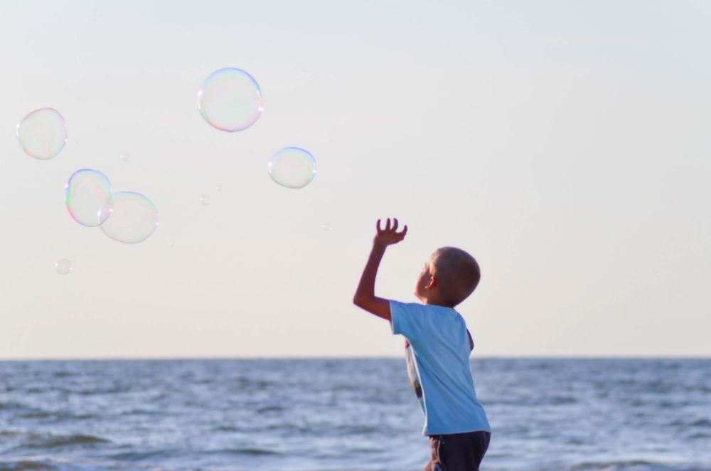 kid playing in the beach with bubbles in the air