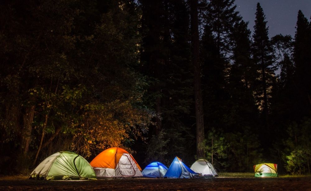 six tents with lights on in the forest at night