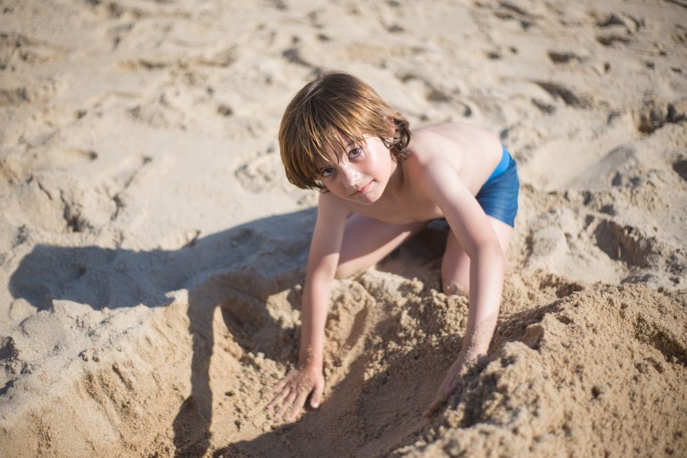 young kid digging sand on the beach and looking at camera