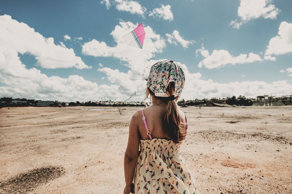 anonymous young girl with a cap flying a kite in the beach