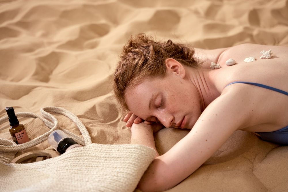 woman sleeps in the beach with rocks on her back near her bag