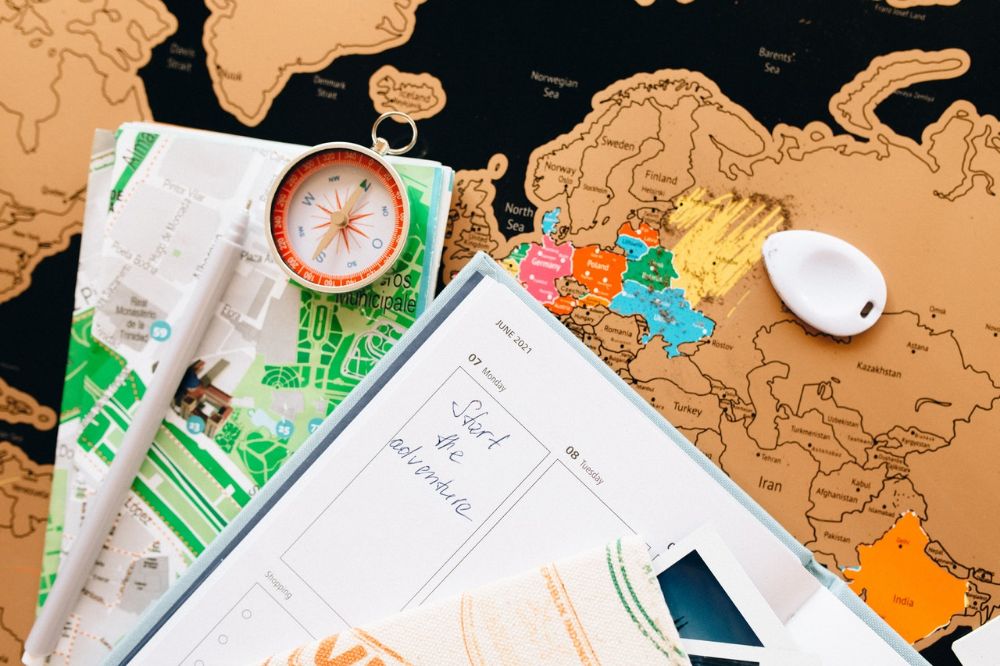 flatlay image of a compass, planner, and travel paraphernalia with the world map as background